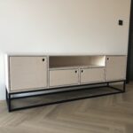 Nowoczesna szafka RTV ATKA wykonana ze sklejki, z przestronnym miejscem na sprzęt multimedialny i dodatkowymi półkami do przechowywania akcesoriów